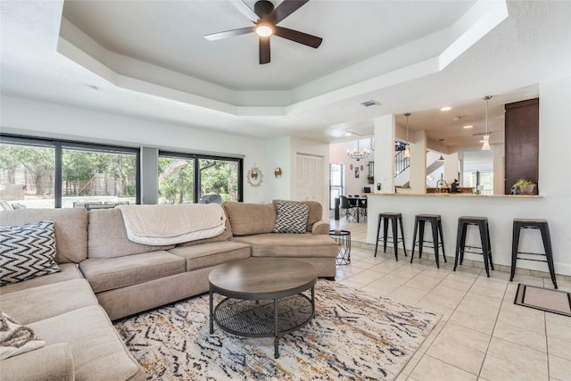 living area with light tile patterned floors, baseboards, visible vents, a raised ceiling, and ceiling fan with notable chandelier