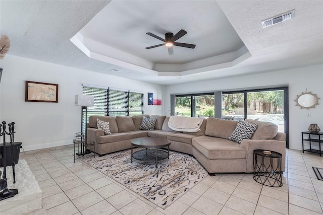 living area featuring light tile patterned floors, a raised ceiling, visible vents, a textured ceiling, and baseboards