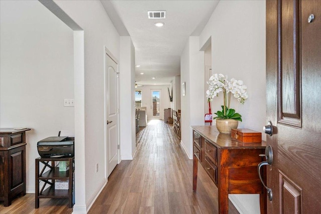 hallway with baseboards, visible vents, and wood finished floors