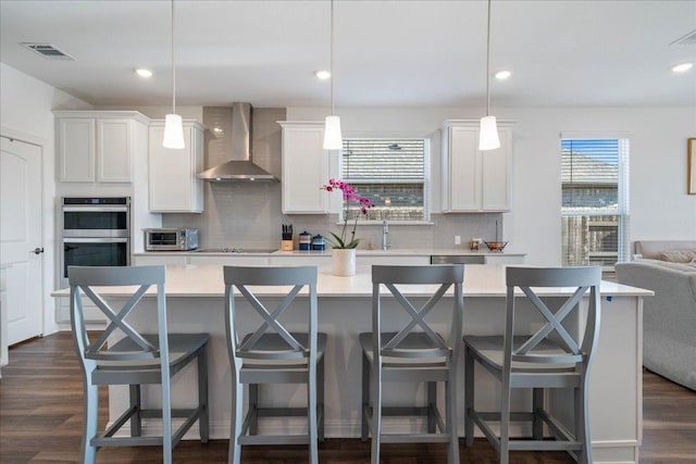 kitchen with wall chimney exhaust hood, visible vents, double oven, and light countertops