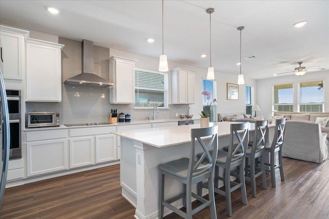 kitchen with open floor plan, black electric stovetop, light countertops, wall chimney range hood, and backsplash