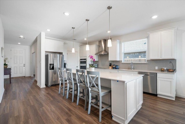 kitchen with dark wood-style floors, appliances with stainless steel finishes, white cabinetry, a kitchen island, and wall chimney exhaust hood