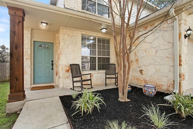 property entrance featuring stone siding, covered porch, and fence