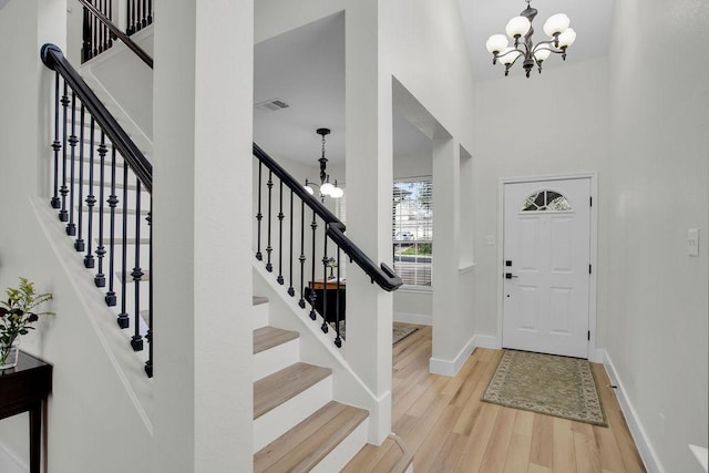 entryway featuring wood finished floors, visible vents, a towering ceiling, and an inviting chandelier