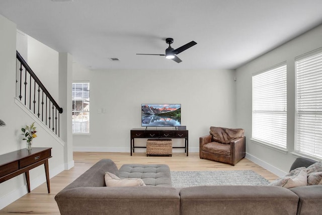 living room featuring baseboards, visible vents, ceiling fan, stairs, and light wood-style floors