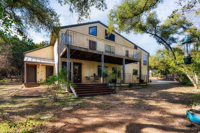 back of house featuring metal roof, a standing seam roof, a balcony, and stucco siding