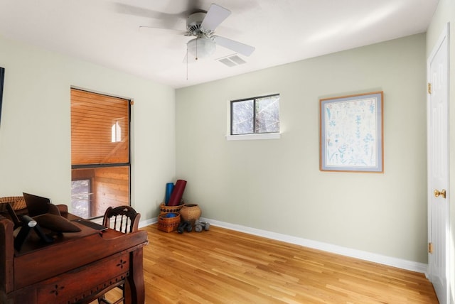 home office with light wood finished floors, a ceiling fan, visible vents, and baseboards