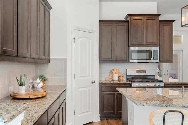 kitchen with appliances with stainless steel finishes, backsplash, light stone counters, and wood finished floors