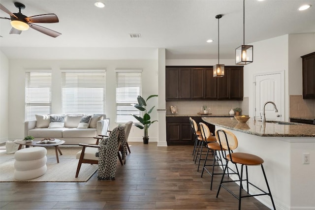 kitchen featuring a breakfast bar area, stone countertops, dark wood-style flooring, a sink, and visible vents