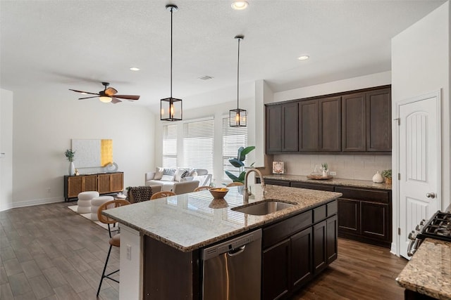 kitchen featuring dark brown cabinetry, stainless steel appliances, a sink, open floor plan, and tasteful backsplash