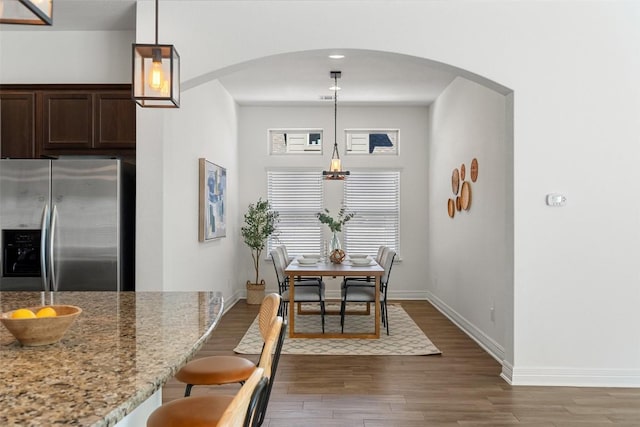 dining space with baseboards, arched walkways, and wood finished floors