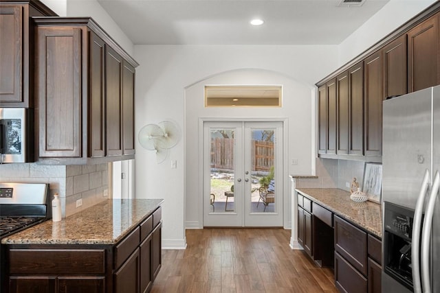 kitchen featuring light stone counters, dark brown cabinetry, wood finished floors, appliances with stainless steel finishes, and decorative backsplash