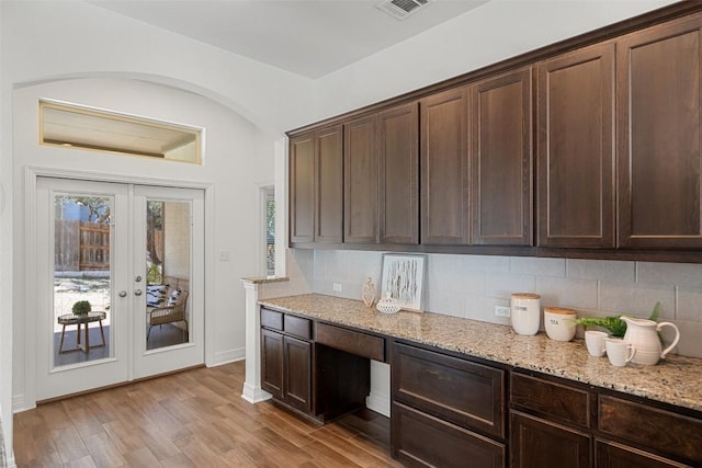 kitchen featuring tasteful backsplash, dark brown cabinetry, light wood-style flooring, and light stone countertops