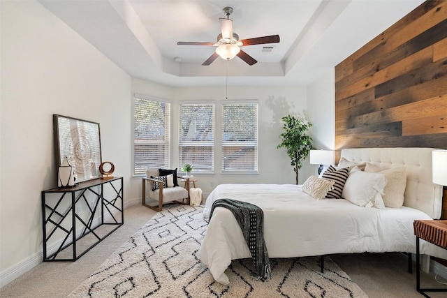 carpeted bedroom featuring a raised ceiling, visible vents, ceiling fan, wooden walls, and baseboards