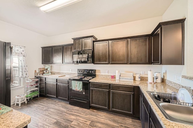 kitchen featuring wood finished floors, dark brown cabinets, black appliances, and a sink