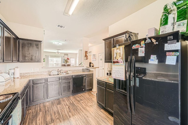 kitchen featuring visible vents, black appliances, dark brown cabinetry, light wood-style floors, and a textured ceiling