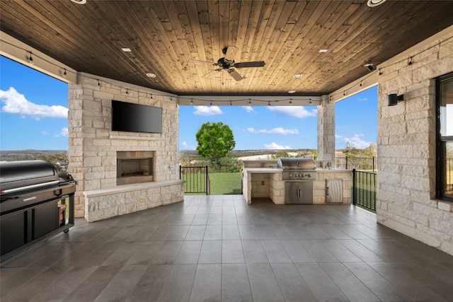 view of patio / terrace with a ceiling fan, an outdoor stone fireplace, a grill, and area for grilling