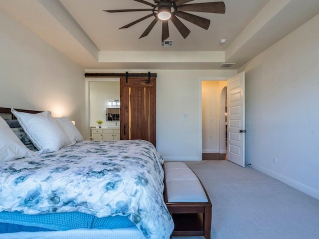 carpeted bedroom featuring arched walkways, a raised ceiling, visible vents, and a barn door