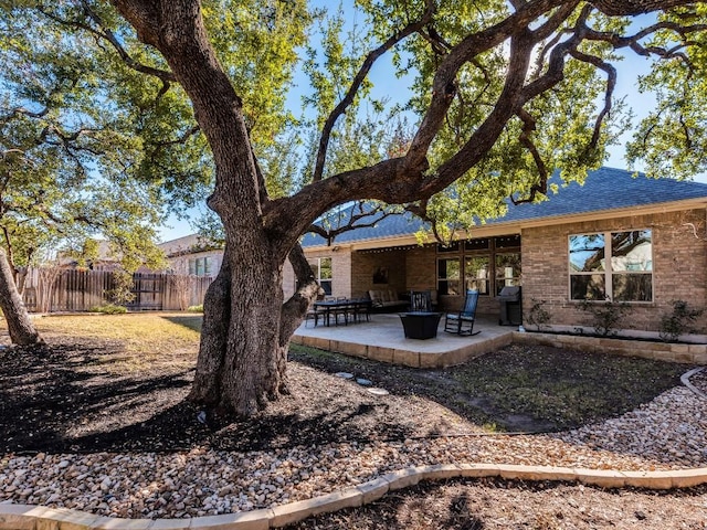 rear view of house with roof with shingles, a patio area, brick siding, and fence