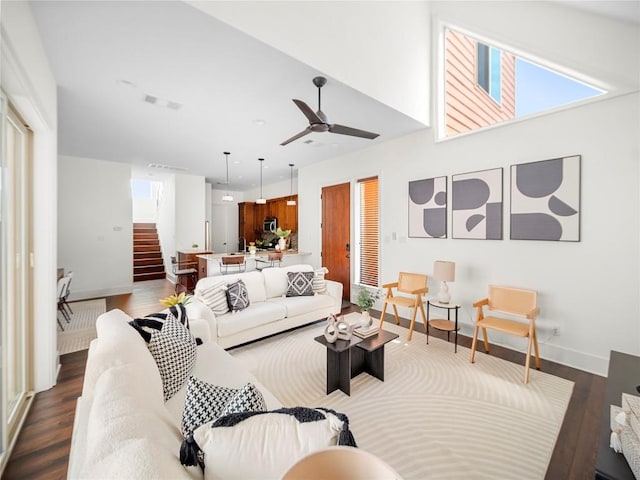 living area with visible vents, baseboards, dark wood-style floors, ceiling fan, and stairs