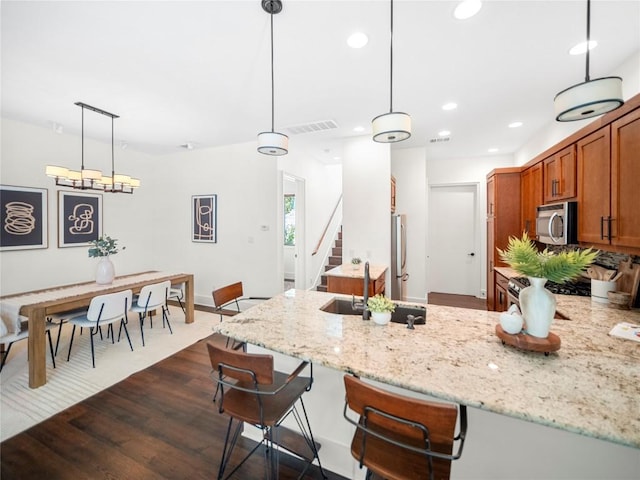 kitchen with brown cabinetry, light stone counters, appliances with stainless steel finishes, a peninsula, and a sink