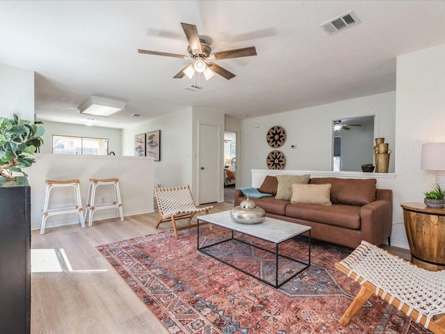 living area with baseboards, ceiling fan, visible vents, and wood finished floors