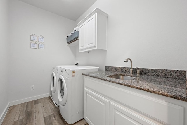 laundry room featuring cabinet space, baseboards, washing machine and clothes dryer, light wood-style floors, and a sink