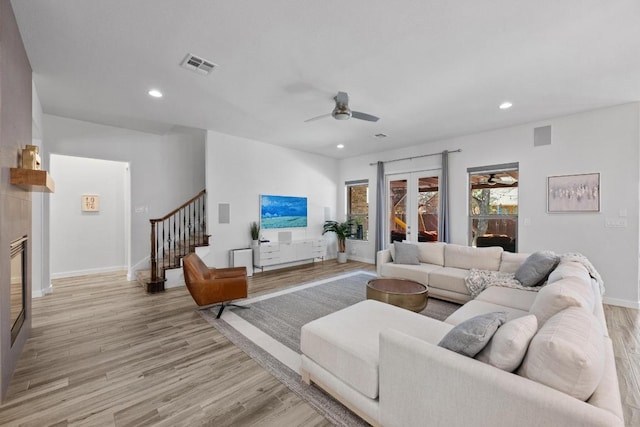 living area with visible vents, a tiled fireplace, stairway, light wood-type flooring, and recessed lighting