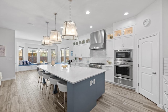 kitchen featuring stainless steel appliances, wall chimney range hood, decorative backsplash, a warming drawer, and a kitchen bar