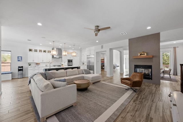 living area featuring recessed lighting, a multi sided fireplace, visible vents, and light wood-style floors