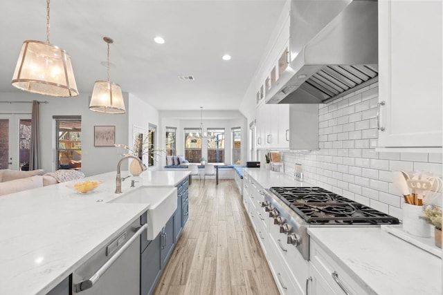 kitchen featuring stainless steel appliances, open floor plan, white cabinetry, a sink, and wall chimney exhaust hood