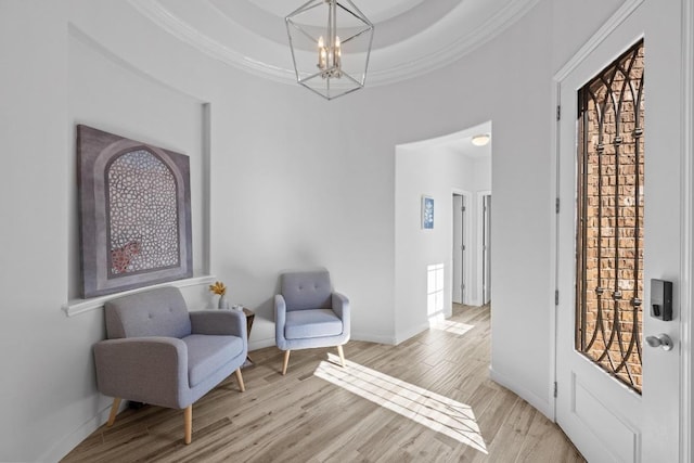 sitting room featuring a chandelier, a raised ceiling, light wood-style flooring, and crown molding