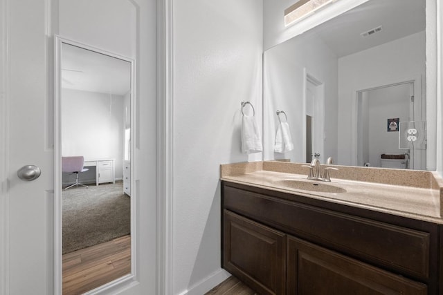 bathroom with visible vents, vanity, baseboards, and wood finished floors