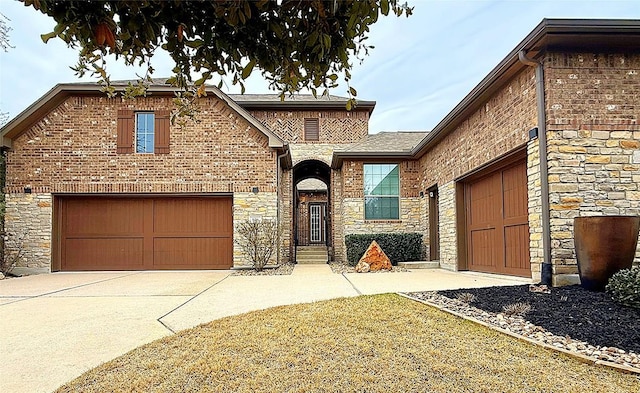 view of front of house featuring a garage, stone siding, brick siding, and driveway