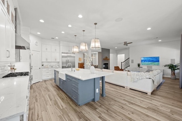 kitchen featuring open floor plan, blue cabinets, stainless steel built in refrigerator, wall chimney range hood, and white cabinetry