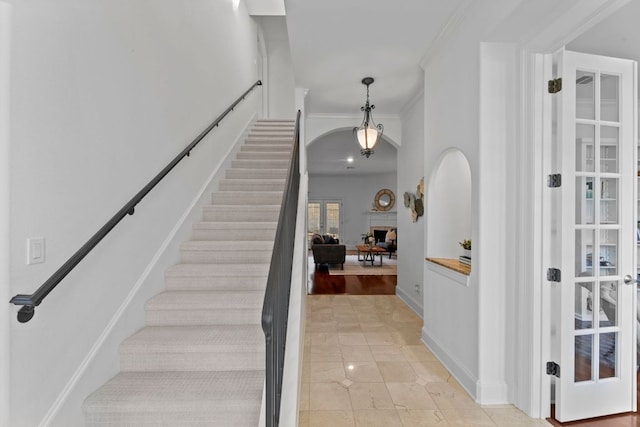 foyer entrance with light tile patterned floors, arched walkways, stairway, crown molding, and a fireplace