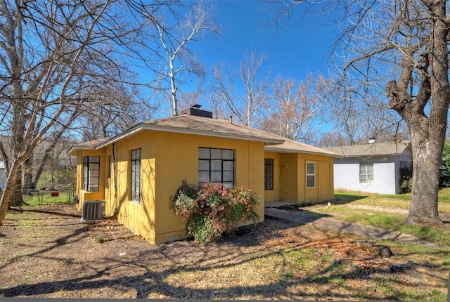 back of property featuring central AC, a chimney, fence, and stucco siding