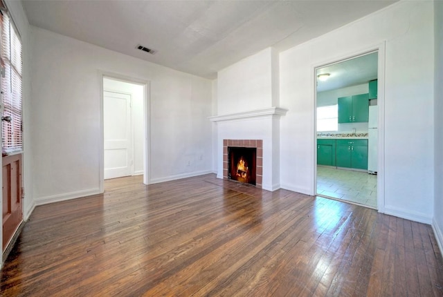 unfurnished living room with dark wood-style flooring, a tiled fireplace, visible vents, and baseboards