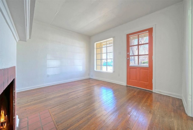 interior space with a warm lit fireplace, baseboards, and hardwood / wood-style flooring