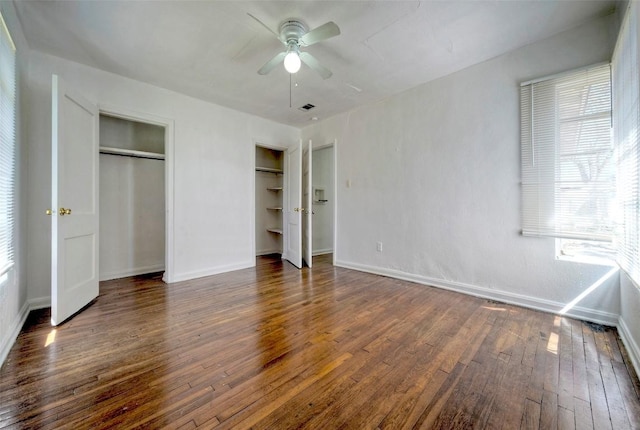 unfurnished bedroom with hardwood / wood-style floors, two closets, visible vents, and baseboards