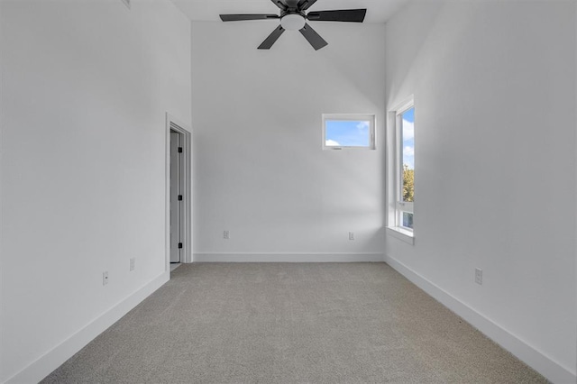 unfurnished room with a ceiling fan, a high ceiling, light colored carpet, and baseboards