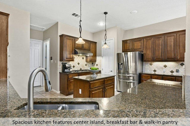 kitchen with under cabinet range hood, stainless steel appliances, a sink, visible vents, and tasteful backsplash