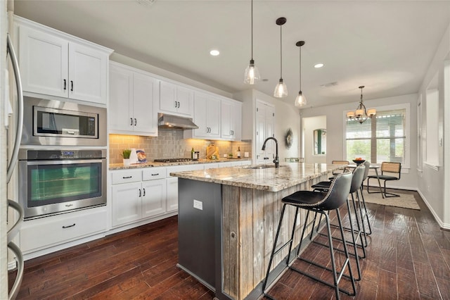 5305 Cardinal Flower Cv, Spicewood, TX 78669 - kitchen featuring appliances with stainless steel finishes, a sink, dark wood-style flooring, light stone counters, and tasteful backsplash