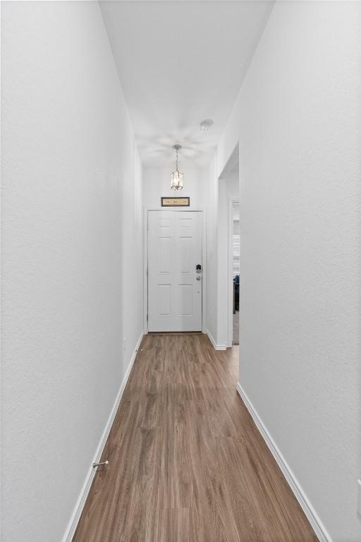 hallway with an inviting chandelier, baseboards, and wood finished floors