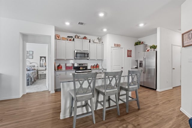 kitchen with a center island with sink, visible vents, a kitchen breakfast bar, wood finished floors, and stainless steel appliances