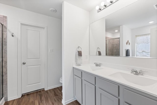 bathroom featuring double vanity, wood finished floors, a sink, and tiled shower