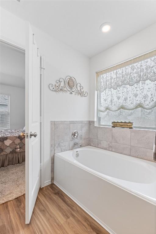 full bathroom with a garden tub, connected bathroom, and wood finished floors