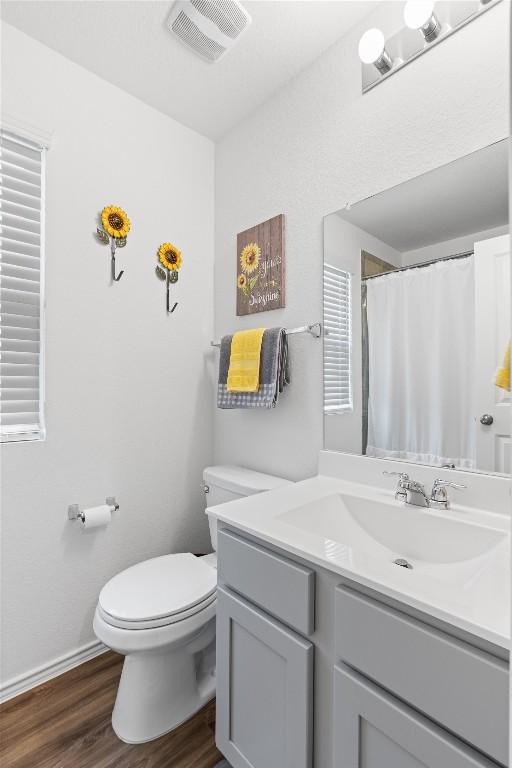 bathroom with visible vents, toilet, vanity, wood finished floors, and baseboards