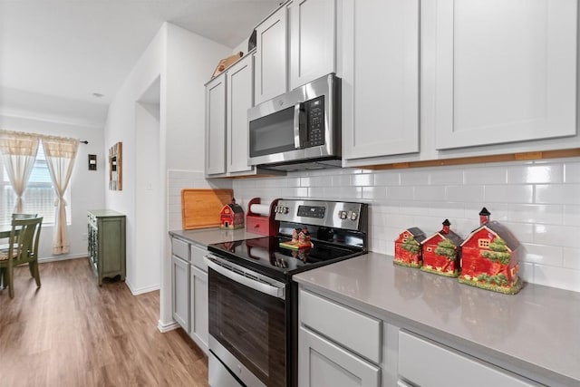 kitchen with light wood finished floors, baseboards, appliances with stainless steel finishes, and decorative backsplash