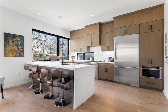 kitchen with a breakfast bar area, a sink, light countertops, tasteful backsplash, and high end appliances